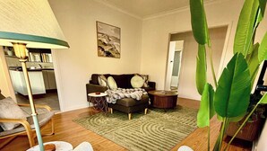 Una sala de estar con sofá, una mesa de centro, una lámpara de pie, una planta grande y un ventilador de techo.