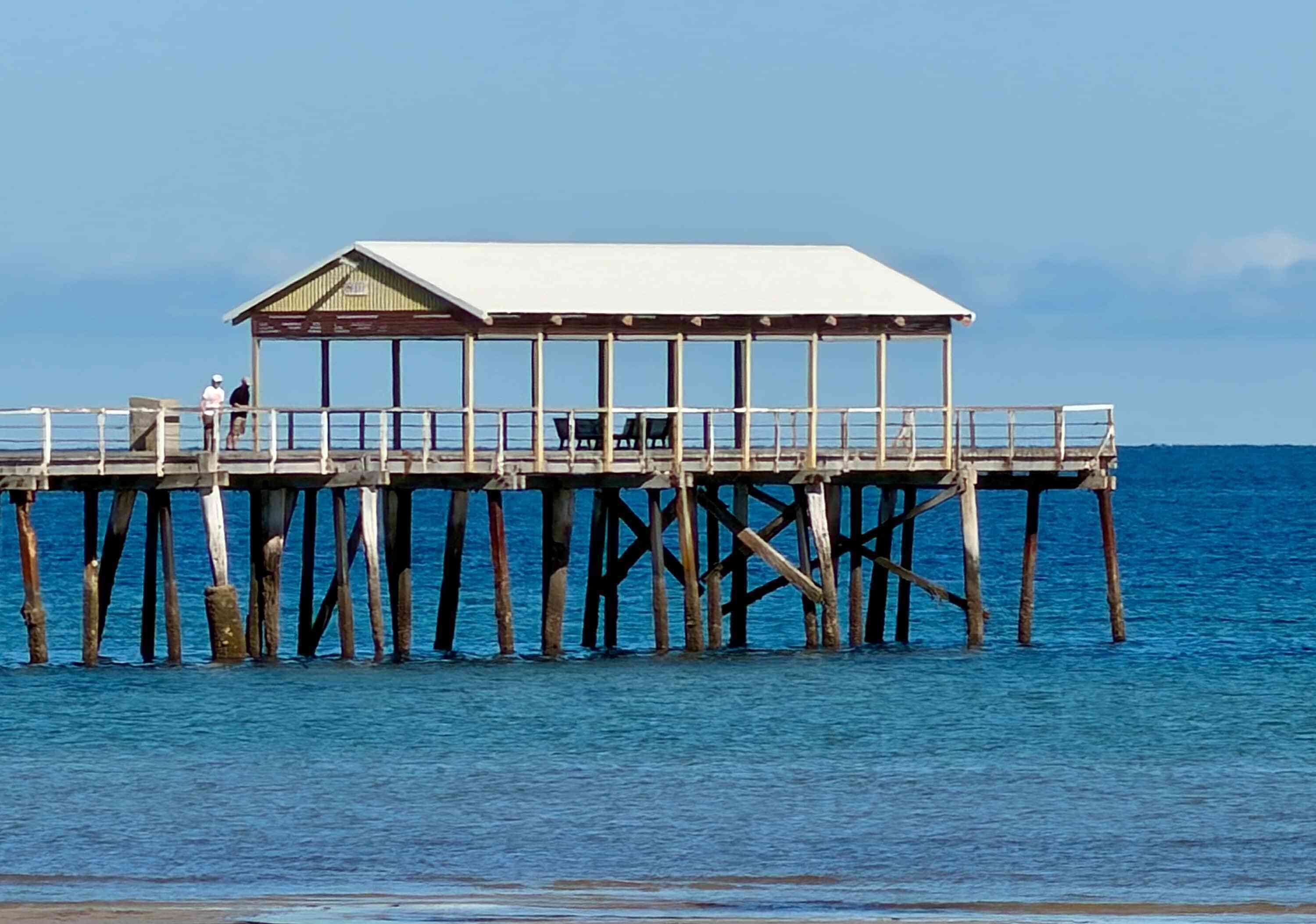 A pier with a covered structure, wooden pillars, and a railing.