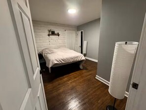 Ein Schlafzimmer mit einem Bett, Holzboden, einer weißen Tür und einer weißen Wand.