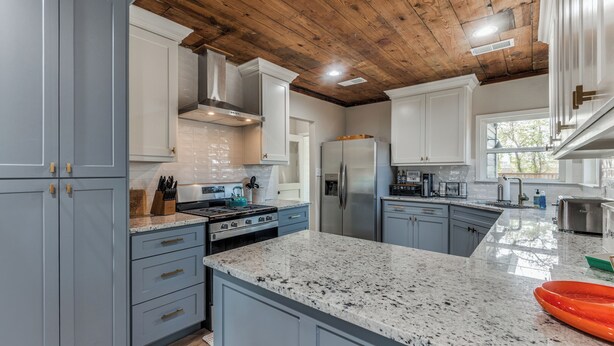 Una cocina con encimeras de granito, electrodomésticos de acero inoxidable y techo de madera.