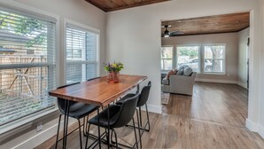 Un comedor con una mesa y sillas de madera, un florero con flores y vistas al exterior a través de grandes ventanales.