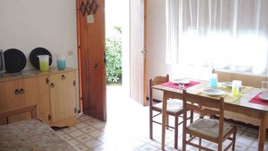 Ein Zimmer mit einem Holzkasten, einem Esstisch mit Stühlen und einer zur Außenseite führenden Tür.