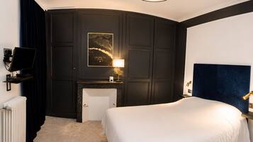 A hotel room with a bed, a desk, a chair, a radiator, a television, and a wall-mounted artwork.