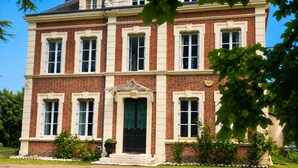 Ein zweistöckiges Backsteingebäude mit zentralem Eingang, großen Fenstern und einer kleinen Gartenanlage.