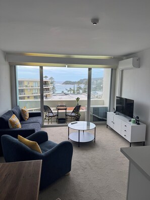 Una sala de estar moderna con un sofá, una mesa de centro, un televisor y un balcón con vista al mar.