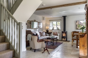 A spacious living room with a fireplace, a sofa, a dining table, and a staircase. - Roundhill Farm Cottage sleeps 2 guests  in 1 bedroom (Naunton)