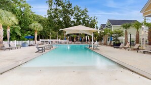 A swimming pool with lounge chairs and umbrellas, surrounded by trees and buildings.