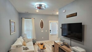 A living room with a sofa, TV, and a kitchen area with granite countertops.