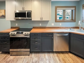 A modern kitchen with stainless steel appliances, wooden countertops, and a window with a view.