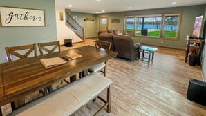 Un área de comedor con una mesa de madera y bancos, un sofá, y un mueble bajo para televisión con un televisor de pantalla plana.