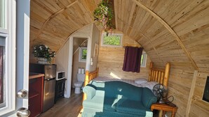 A cozy attic bedroom with a wooden ceiling, a green sofa, a bed, a small table, and a hanging plant.