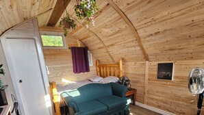 A cozy attic bedroom with a wooden ceiling, a bed with a headboard, a window, and a wall-mounted fan.