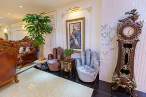An opulent room with a grand piano, plush armchairs, a large ornate clock, and a framed peacock painting. - Queen T and T Dalat (Da Lat)