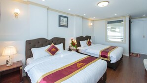 A hotel room with two beds, a nightstand with a lamp, a framed picture on the wall, and a window with a view. - Queen T and T Dalat (Da Lat)