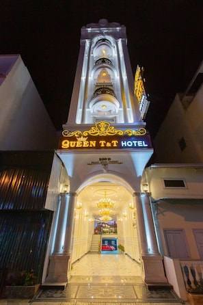Entrada d'hotel amb un arc monumental, un candelabro i un rètol que diu 'QUEEN T&T HOTEL'.