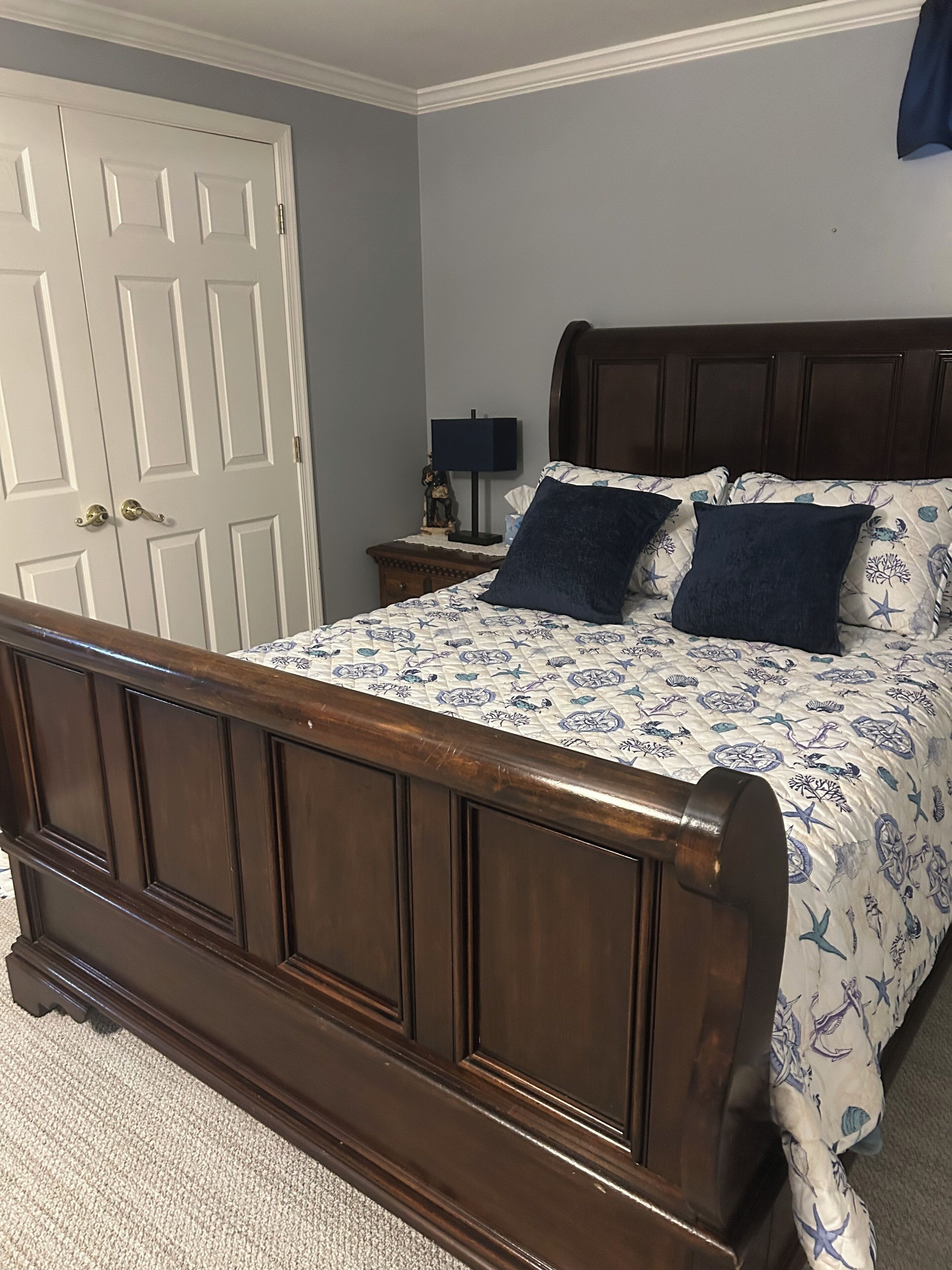 A bedroom with a wooden bed, a nightstand, a lamp, and a closed door.