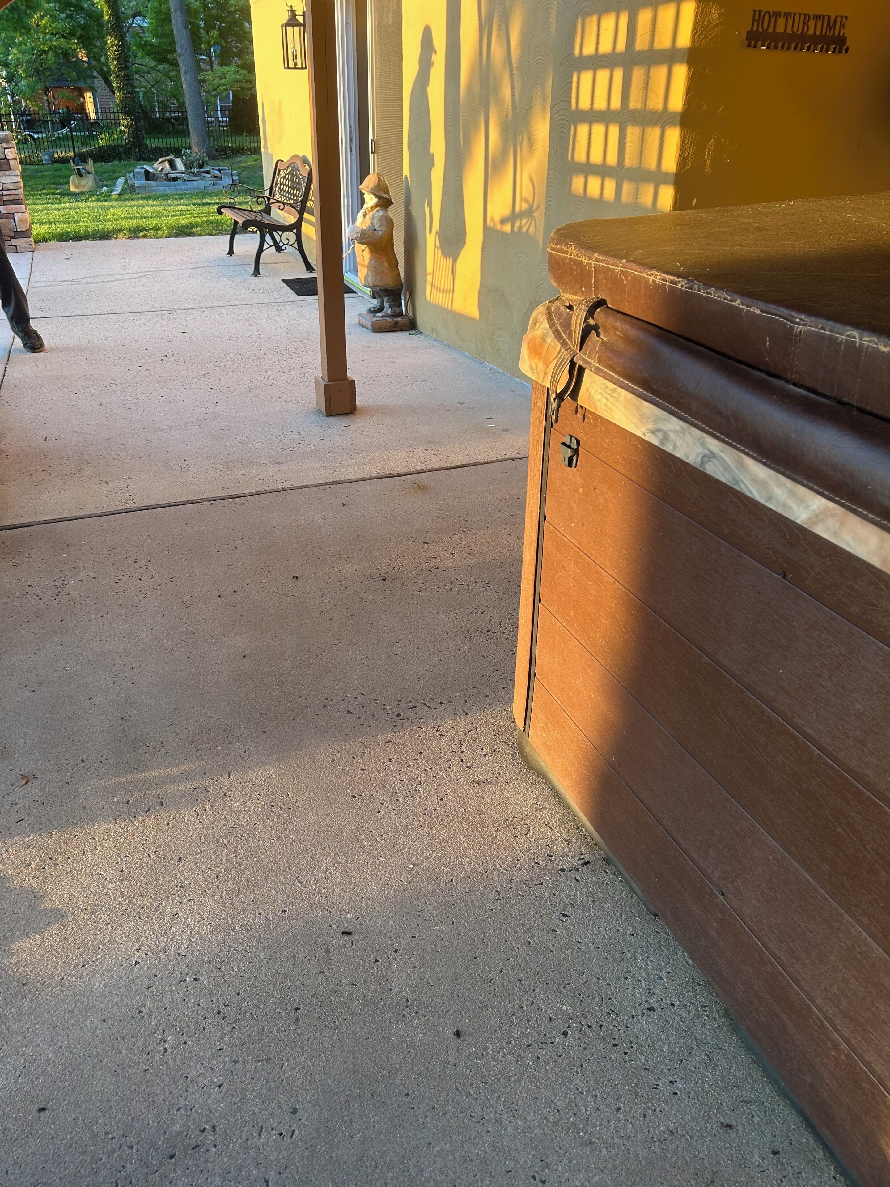 Une terrasse en béton avec un banc, une statue et un mur jaune sur lequel se projette une ombre.