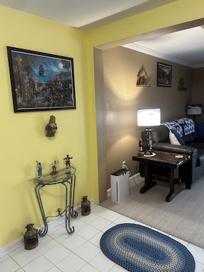 A living room with a yellow wall, a painting, a glass table with figurines, a black leather sofa, and a blue rug. - WATERFRONT, PIER, HOT TUB, FIRE TABLE, KAYAKS, AIR HOCKEY, 1 LEVEL (Aberdeen)
