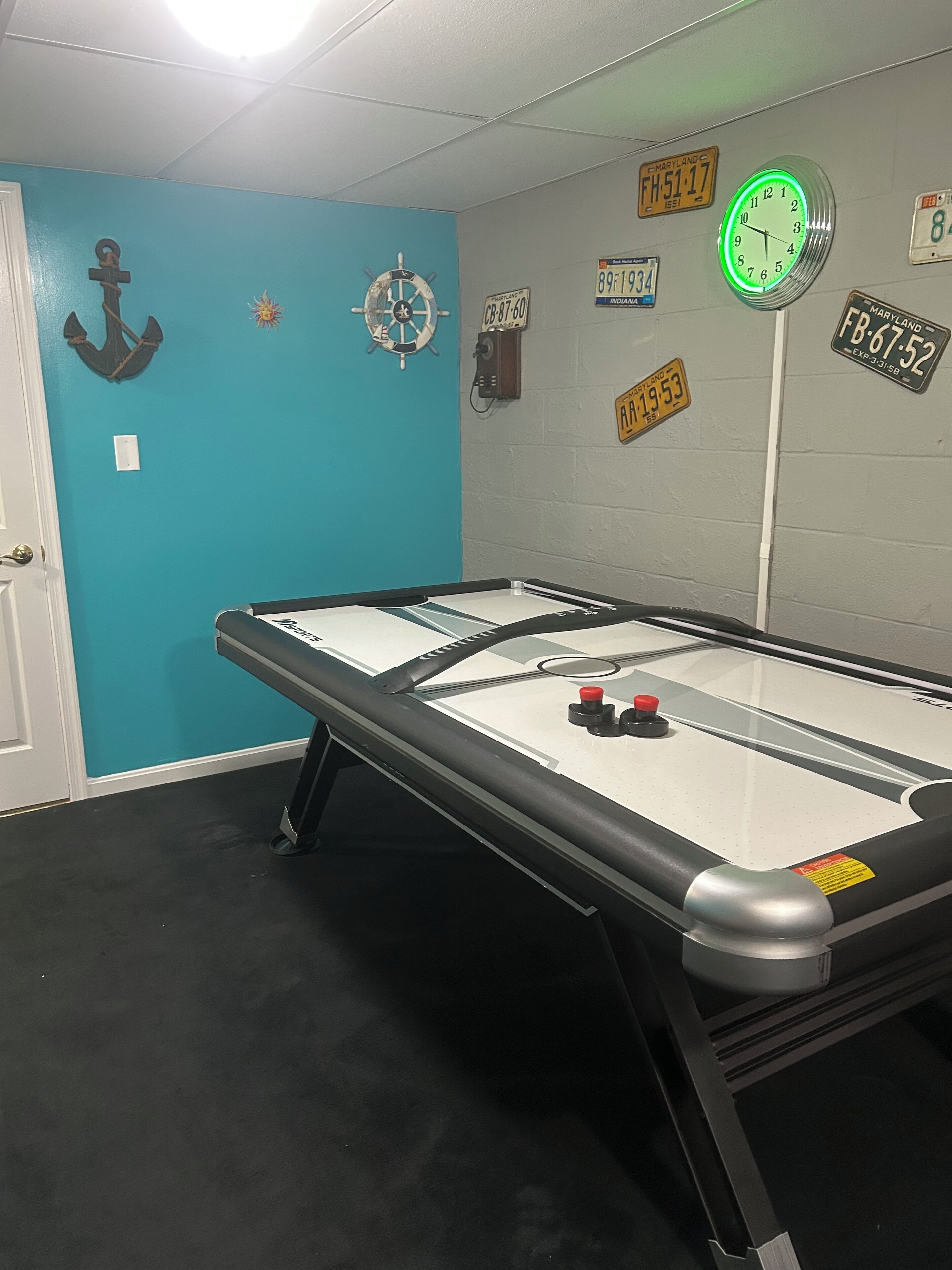 A room with a shuffleboard table, a clock, and several license plates on the wall.