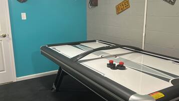 A room with a shuffleboard table, a clock, and several license plates on the wall.