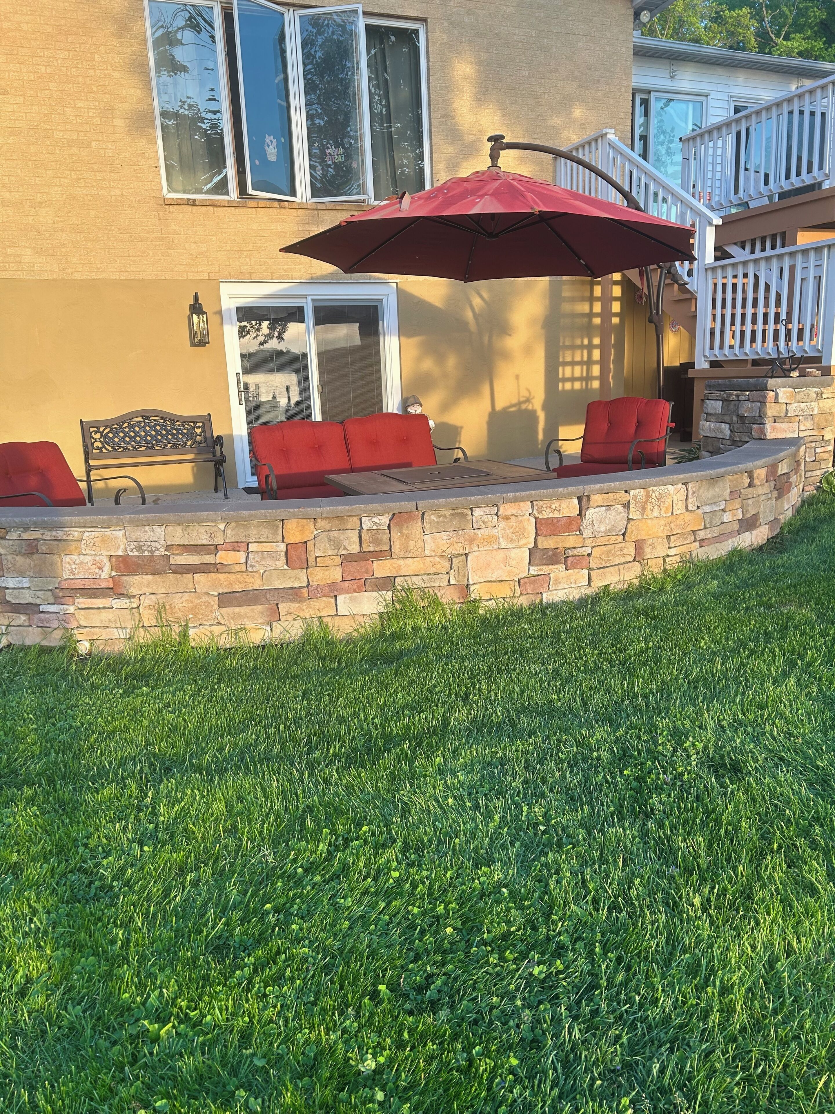 A patio with a stone wall, a bench, and a red umbrella.