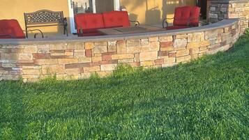 A patio with a stone wall, a bench, and a red umbrella.