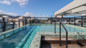 A rooftop swimming pool with clear blue water, surrounded by a wooden deck and metal railings. - Complete Loft - New Campeche. Swimming pool, gym, laundry facilities, and close to the beach. (Florianópolis)