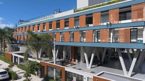 A modern multi-story building with a flat roof, large windows, and a mix of wooden and metal railings. - Complete Loft - New Campeche. Swimming pool, gym, laundry facilities, and close to the beach. (Florianópolis)
