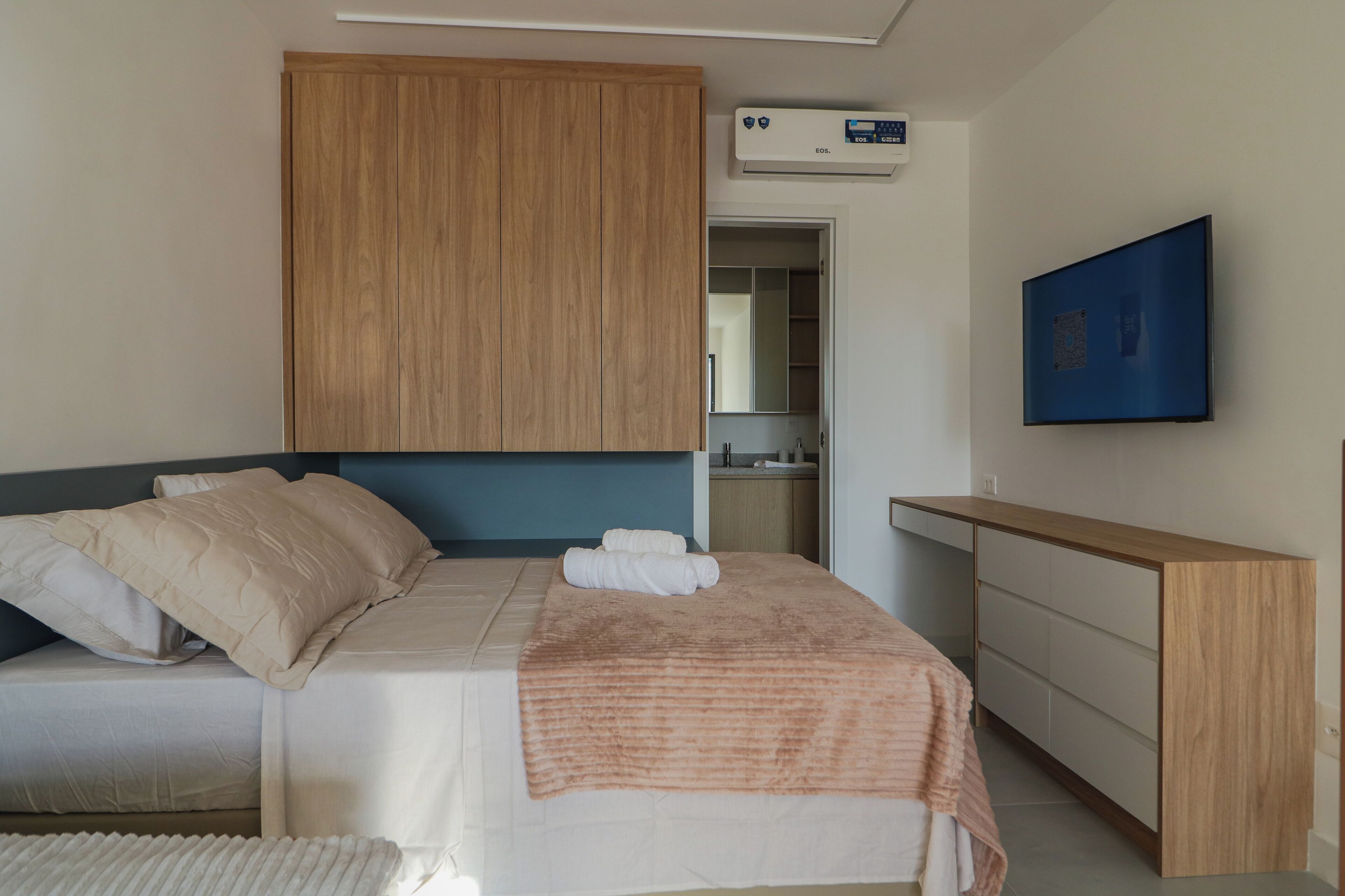 Une chambre à coucher comprenant un lit, une armoire en bois, une salle de bain avec un miroir et un téléviseur à écran plat fixé au mur.