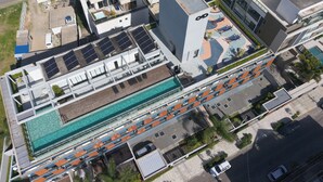 An aerial view of a modern building with a swimming pool, solar panels, and outdoor seating areas. - Complete Loft - New Campeche. Swimming pool, gym, laundry facilities, and close to the beach. (Florianópolis)