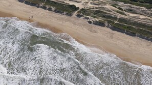 A beach with waves crashing onto the shore, a sandy path, and some greenery. - Complete Loft - New Campeche. Swimming pool, gym, laundry facilities, and close to the beach. (Florianópolis)