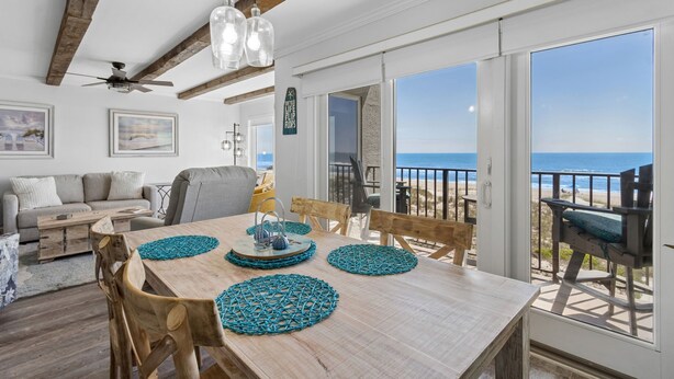 A dining area with a wooden table, chairs, and a view of the ocean through large sliding glass doors.