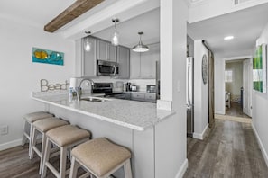 A kitchen with a central island, bar stools, a microwave, and a refrigerator.