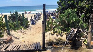 Une plage avec une promenade en bois menant à l’océan, entourée de cactus et agrémentée d’un panneau indiquant la présence d’une laverie.