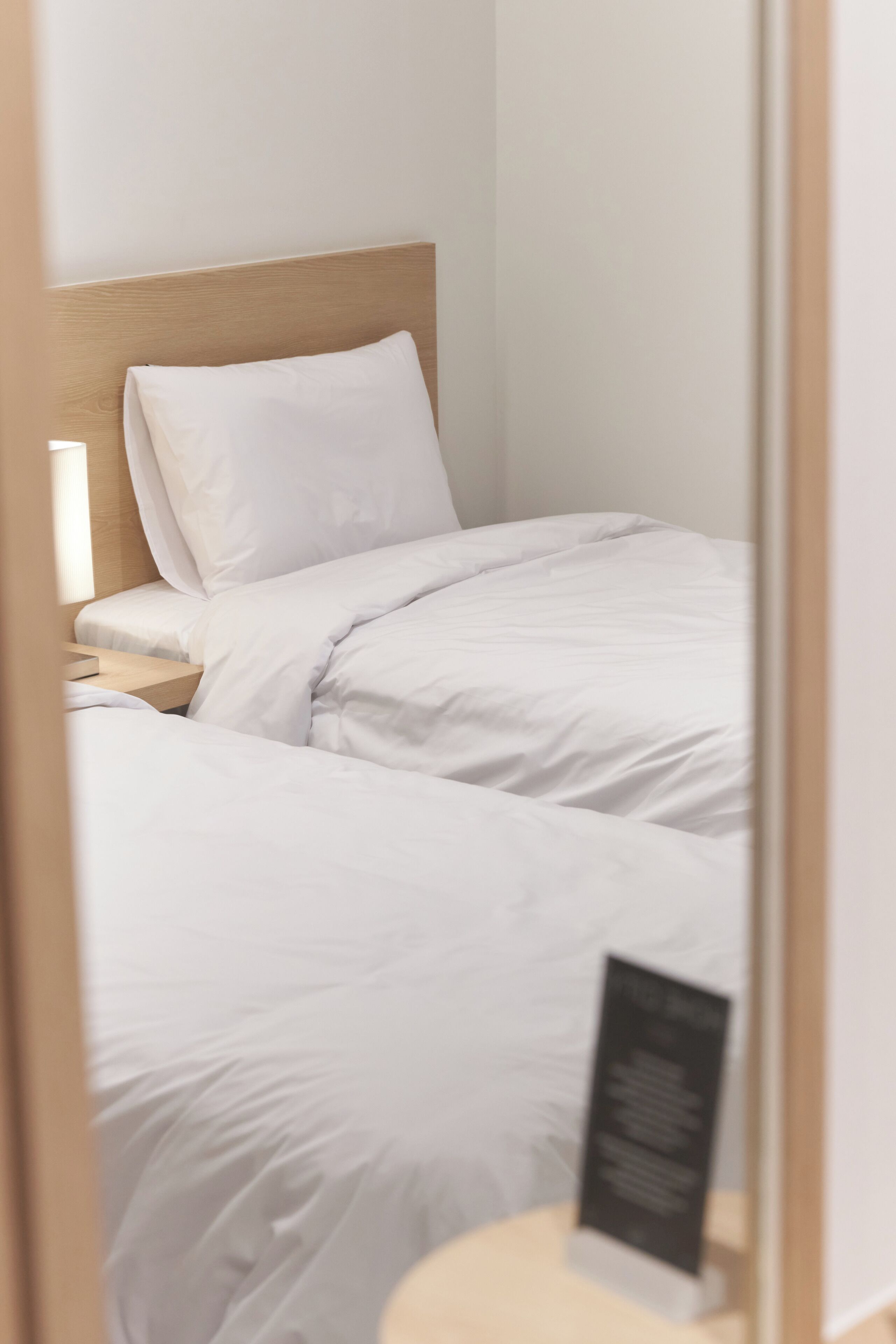 Habitación de hotel con dos camas, una mesita de noche y otra mesita auxiliar.