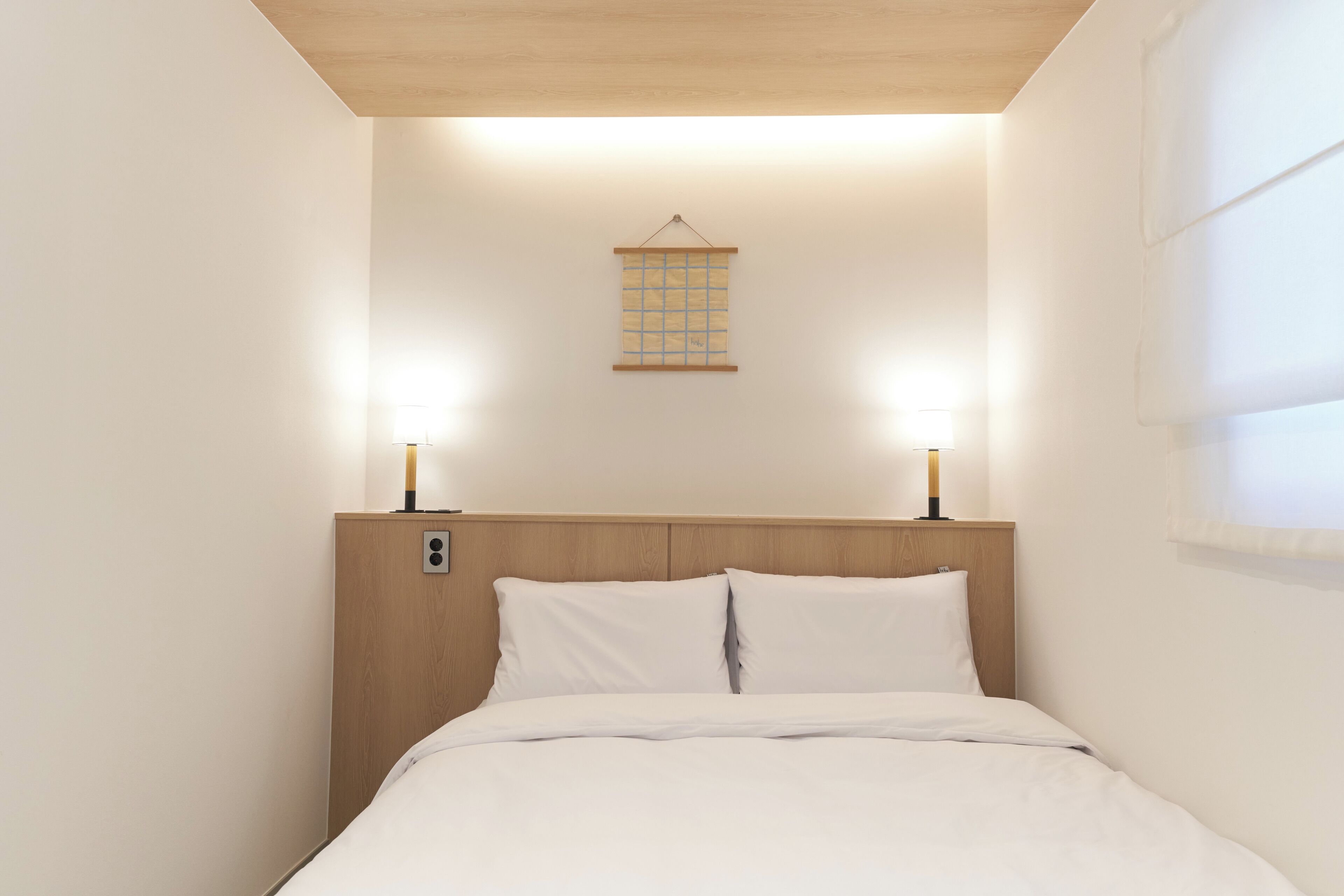 A neatly made bed with white linens, a wooden headboard, and two bedside lamps.