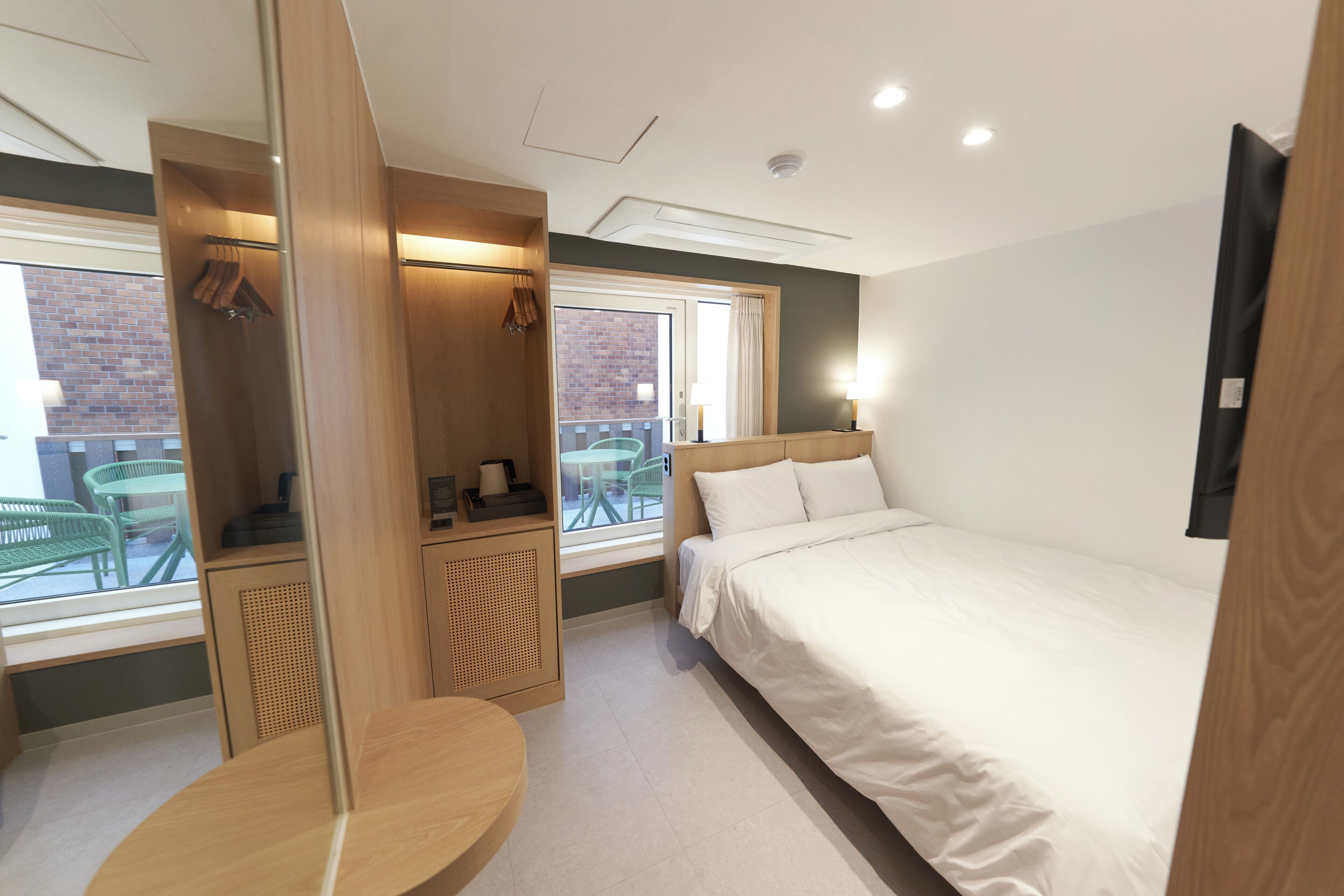A modern hotel room with a bed, a small table, a seating area, and a window with a view of the outside.