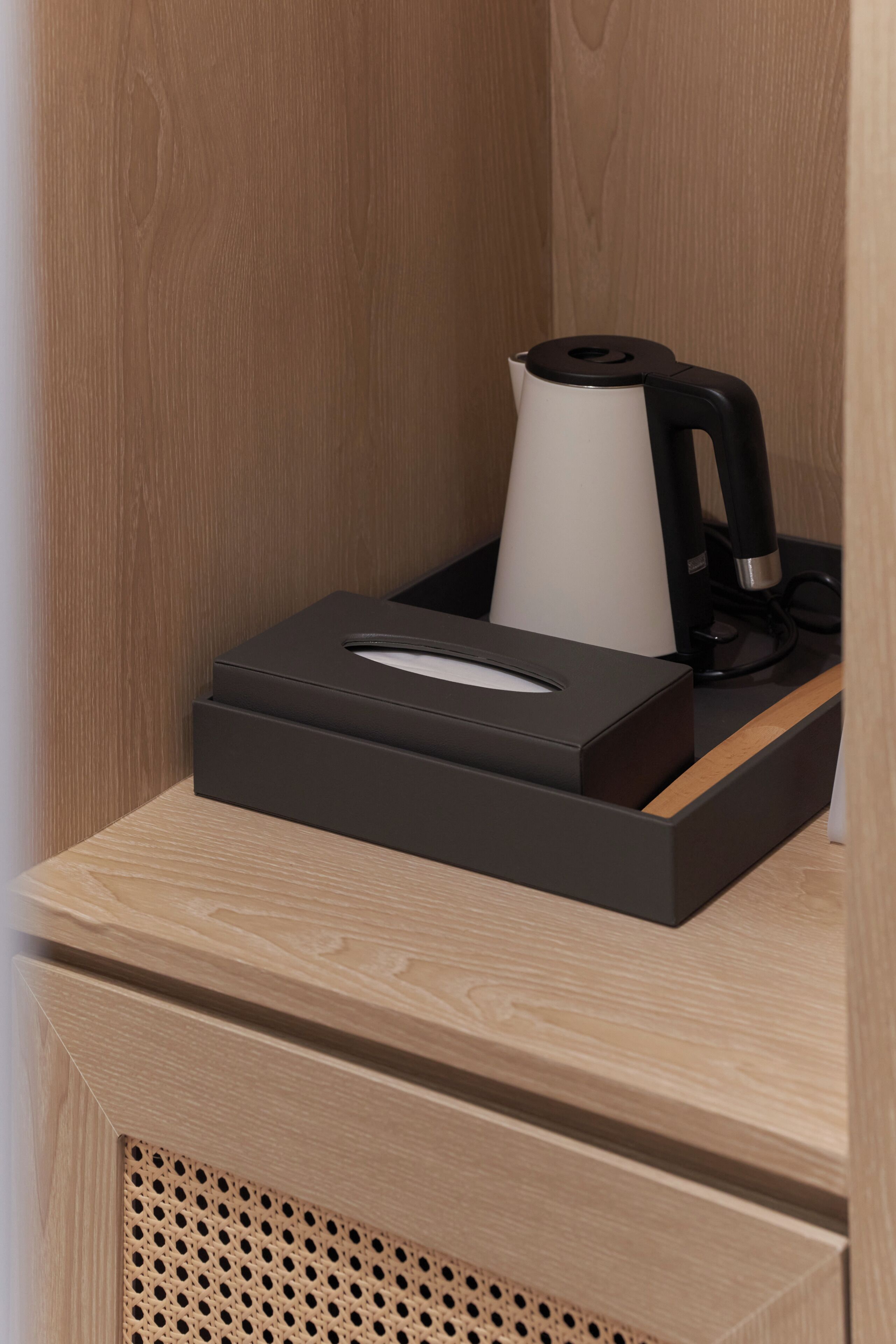 A wooden bedside table with a black tissue box and a white kettle.