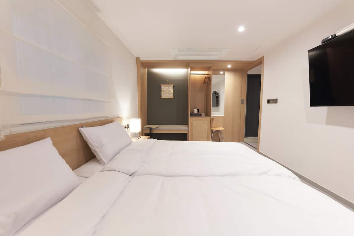 A hotel room with a large bed, a bedside table, a lamp, a TV mounted on the wall, and a mirror.