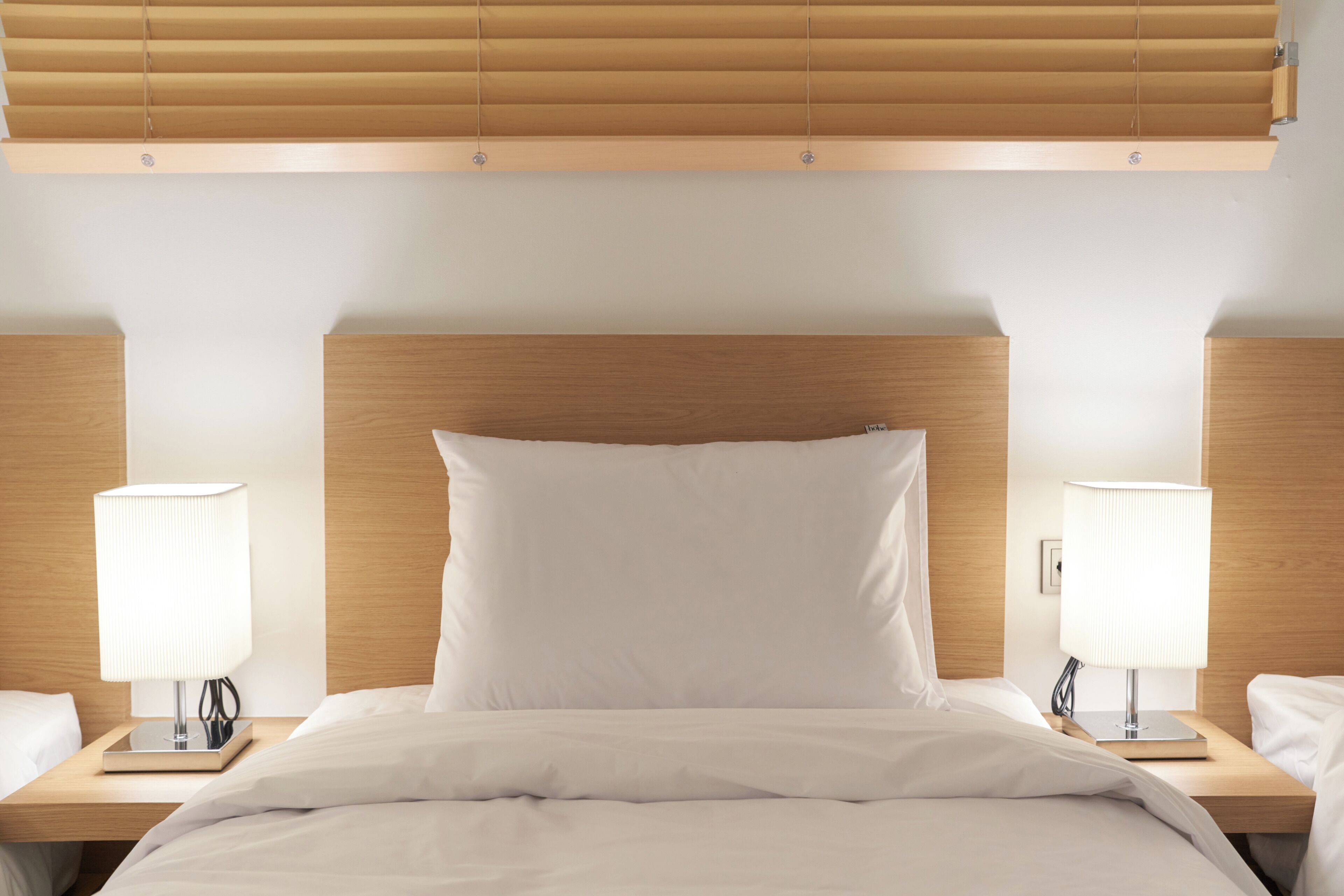 A hotel room with a wooden headboard, two bedside tables with lamps, and a bed with white bedding.