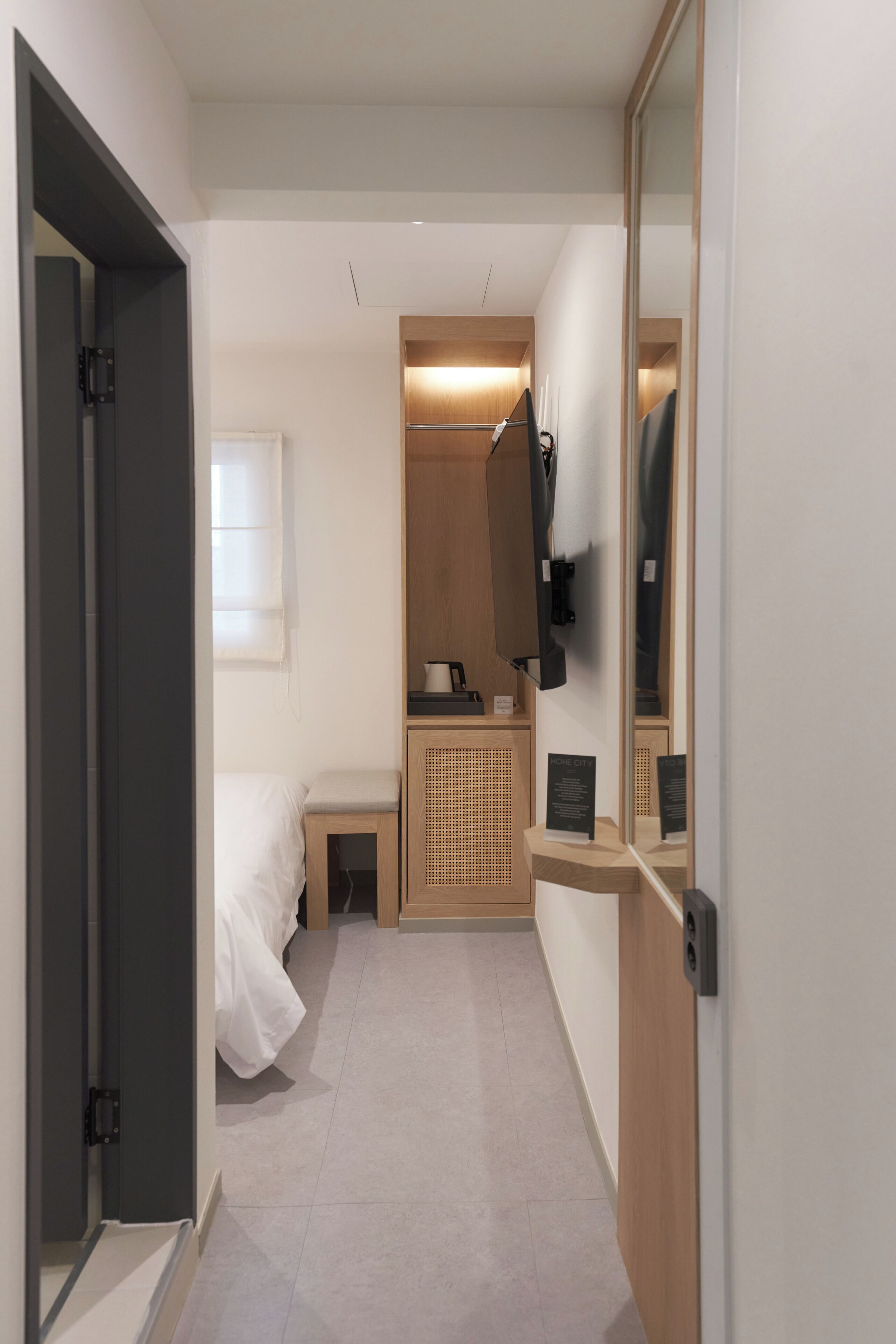 Une chambre d’hôtel de taille réduite, comprenant un lit, un petit bureau, un miroir et une armoire.