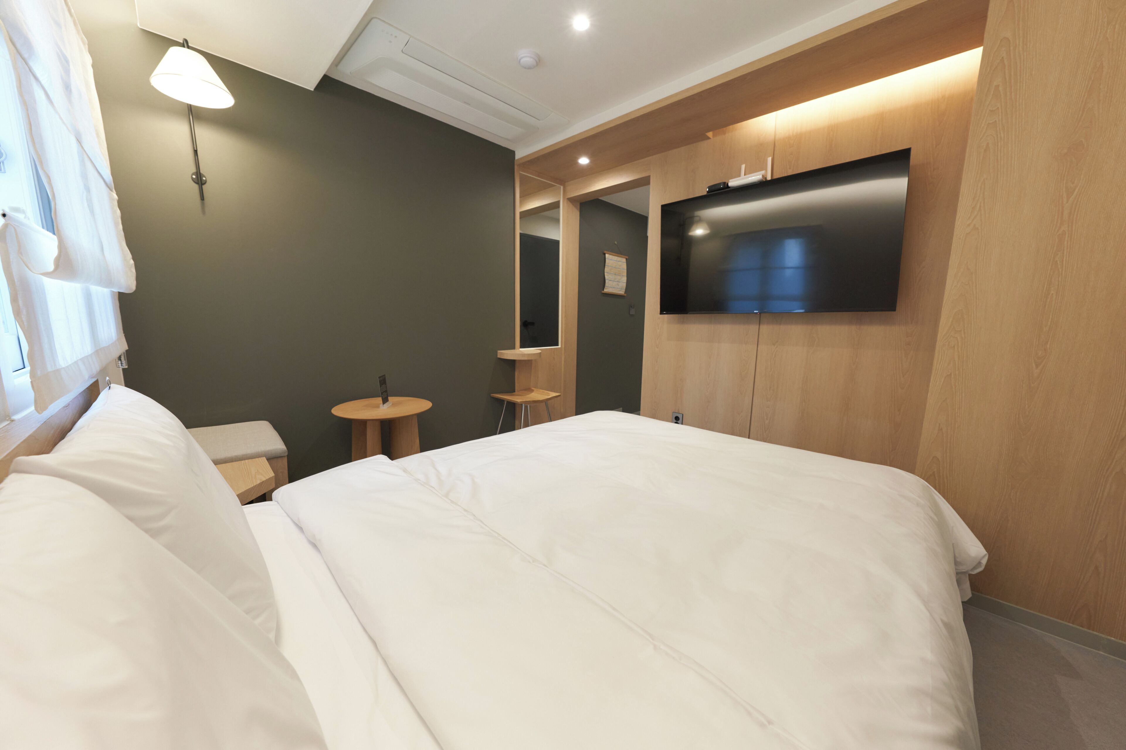 A hotel room with a bed, a TV mounted on the wall, a small table, and a lamp.
