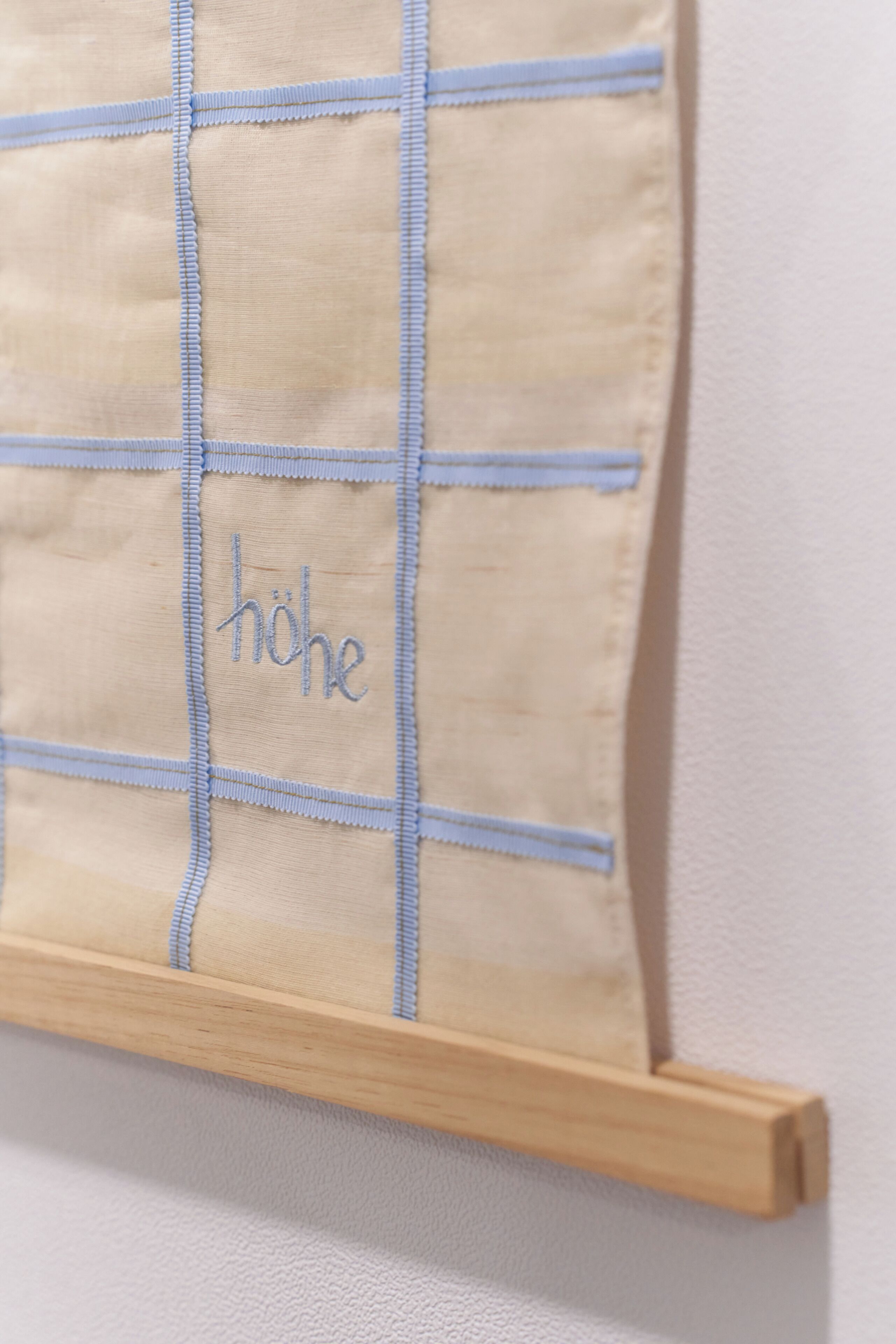 Tejido beige con pespuntado azul y la palabra 'höhe' bordada.