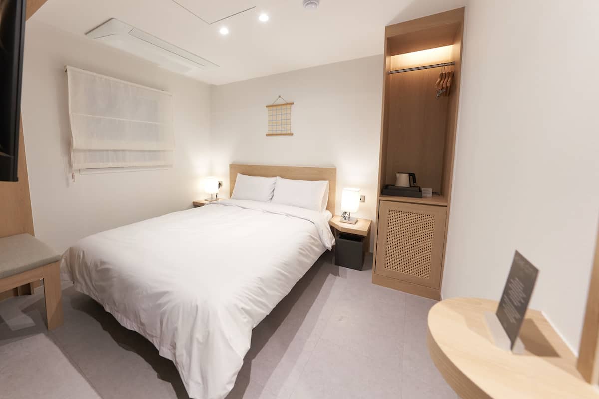 A hotel room with a large bed, bedside tables, a bench, a wardrobe, and a mirror.