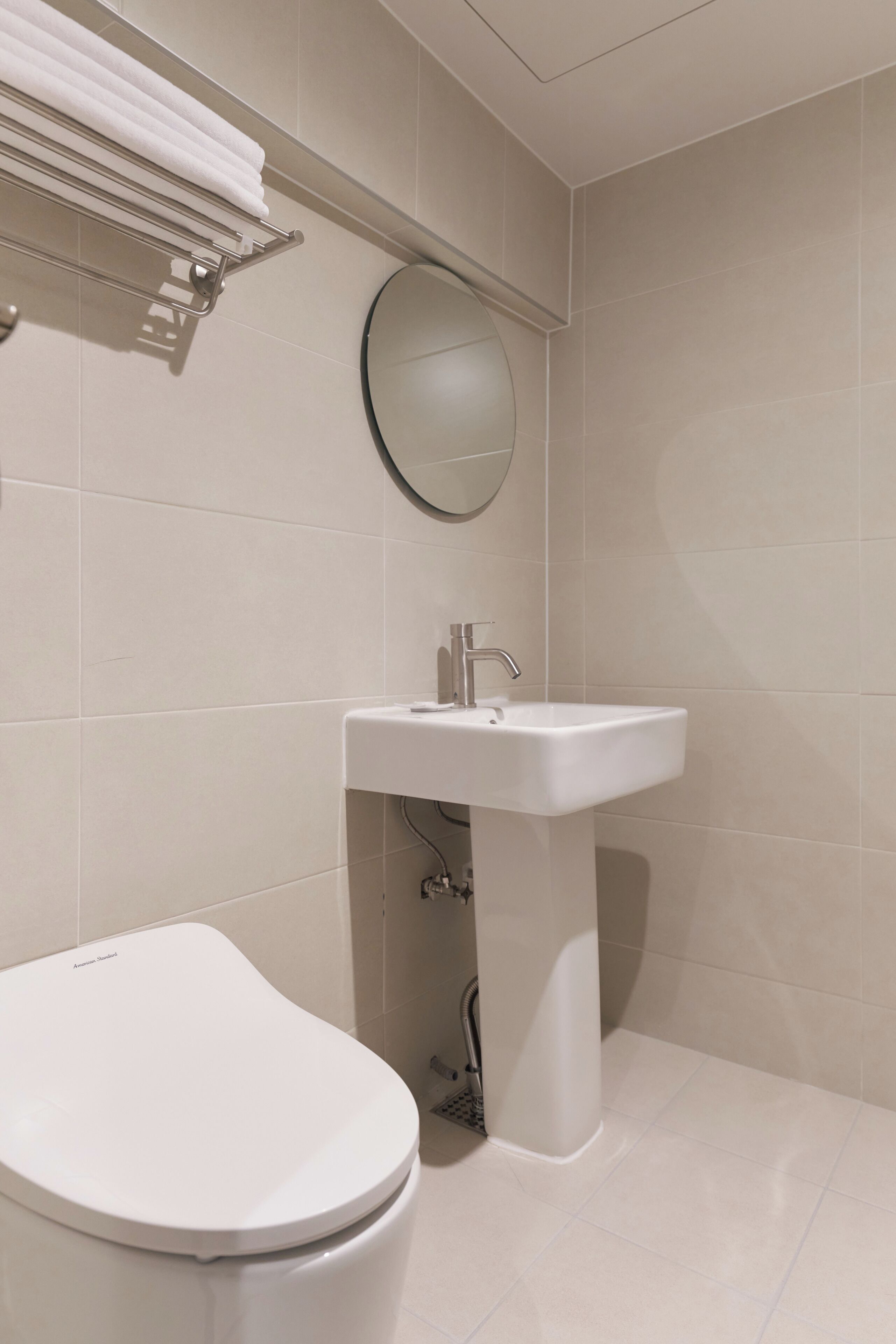 A bathroom with a white toilet, a pedestal sink, a towel rack, and a mirror.
