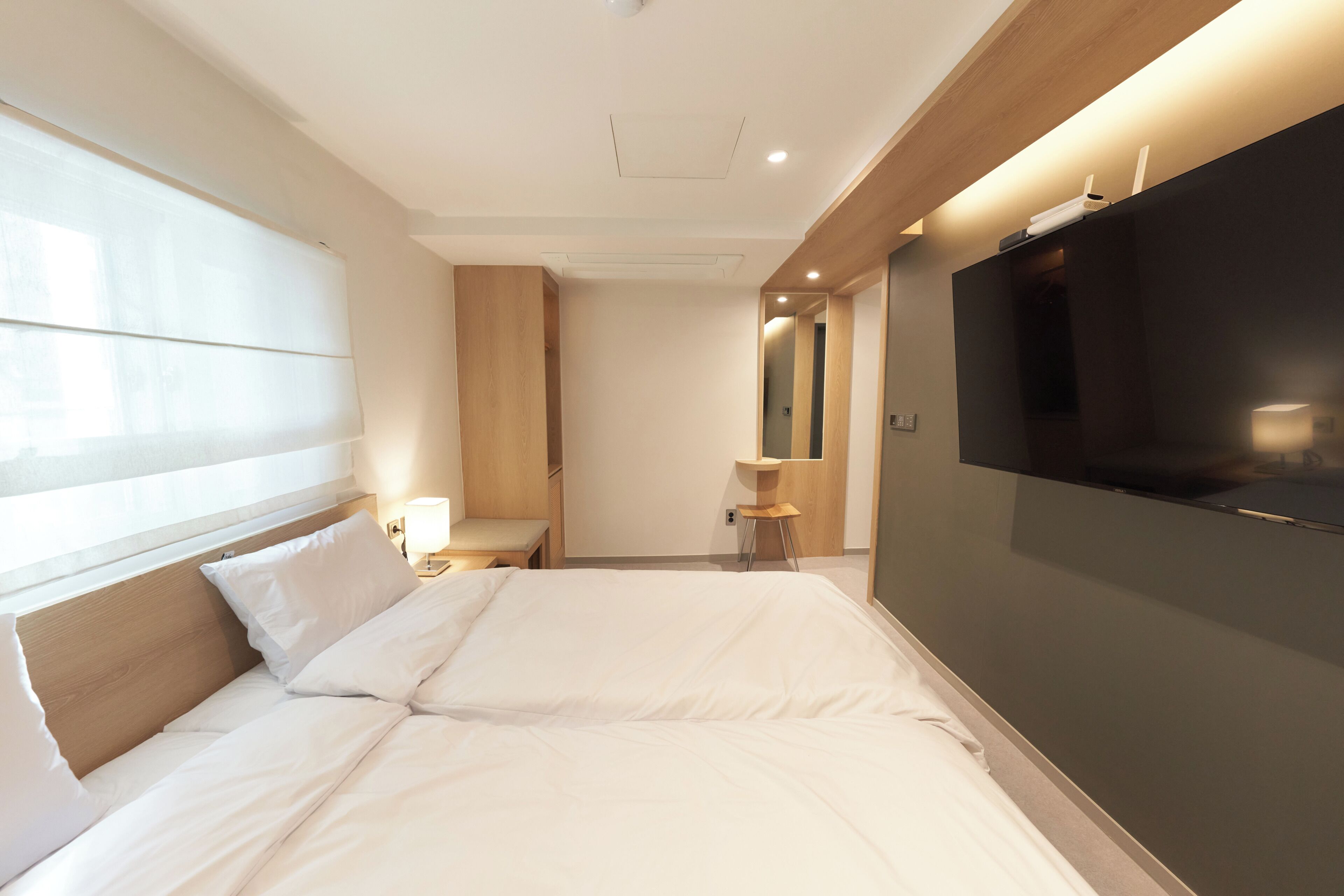 Une chambre d’hôtel moderne avec un grand lit, un téléviseur à écran plat, une tête de lit en bois, une petite table et un miroir.