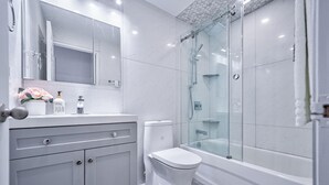 Un baño moderno con ducha de vidrio, inodoro blanco y tocador con espejo y dispensador de jabón.