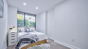Un dormitorio con cama, ventana, lámpara y una planta pequeña.