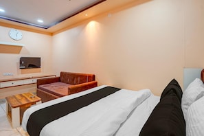 A hotel room with a bed, a TV, a clock, a desk, and a seating area. - Classic Hotel Ramashray Palace (Ujjain)