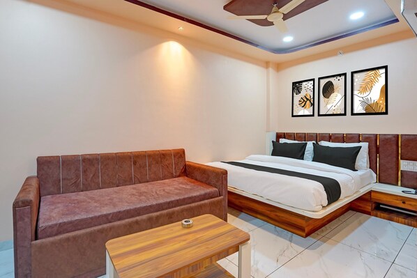A room with a bed, a brown sofa, a small wooden table, and three framed leaf artworks on the wall. - Classic Hotel Ramashray Palace (Ujjain)